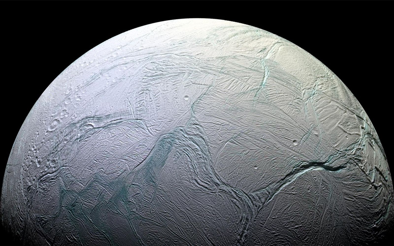 A half circle, with turquoise cracks across the left side its pale blue surface. Craters are shown along its middle and lower right sides.
